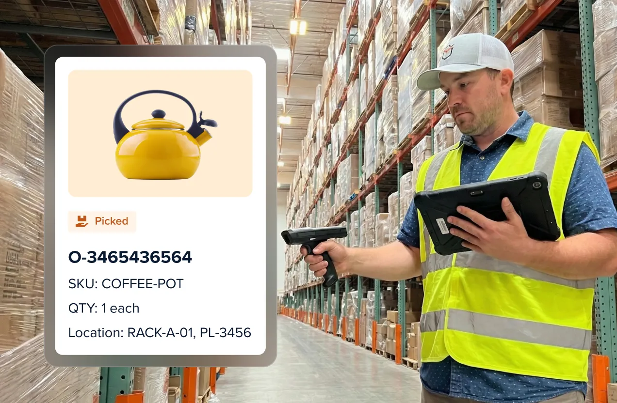 Warehouse worker in a yellow safety vest and cap scans inventory using a barcode scanner and tablet in an aisle with tall shelves stocked with boxes.
