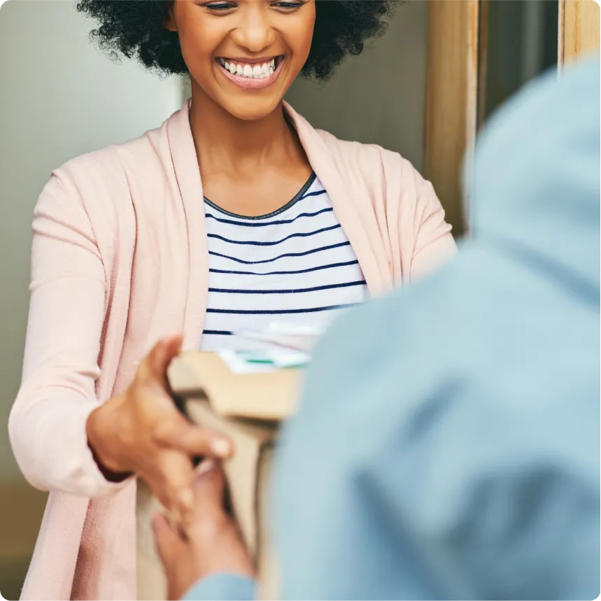 Smiling woman receiving a delivery package from a person in a blue jacket.