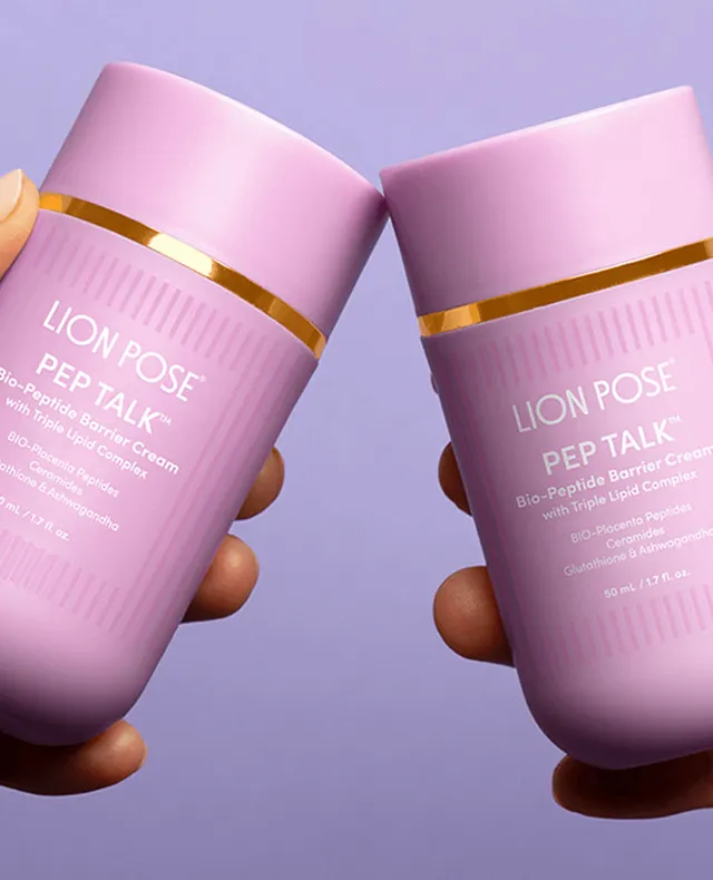 Two hands holding pink bottles of Lion Pose PEP TALK Bio-Peptide Barrier Cream with Triple Lipid Complex against a solid light purple background.