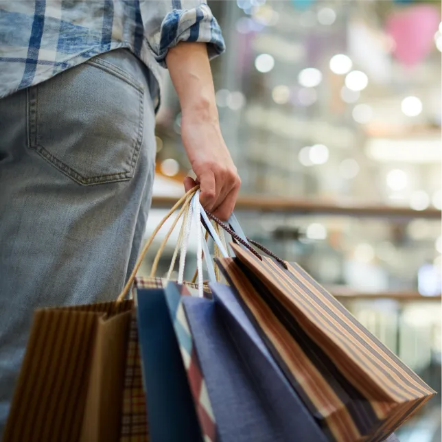 Person wearing jeans and a plaid shirt holding several shopping bags in a mall.