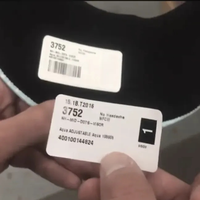 Two white product labels held near a black item, one label shows item number 3752, description Aqua Adjustable Aqua 1980s, and barcode.