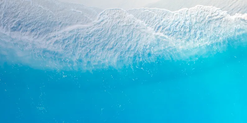 Aerial view of clear turquoise ocean water with gentle white waves breaking near the shore.
