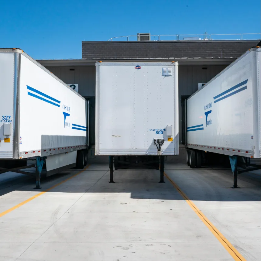 Three white Cascade trailers parked at loading docks under a clear blue sky.