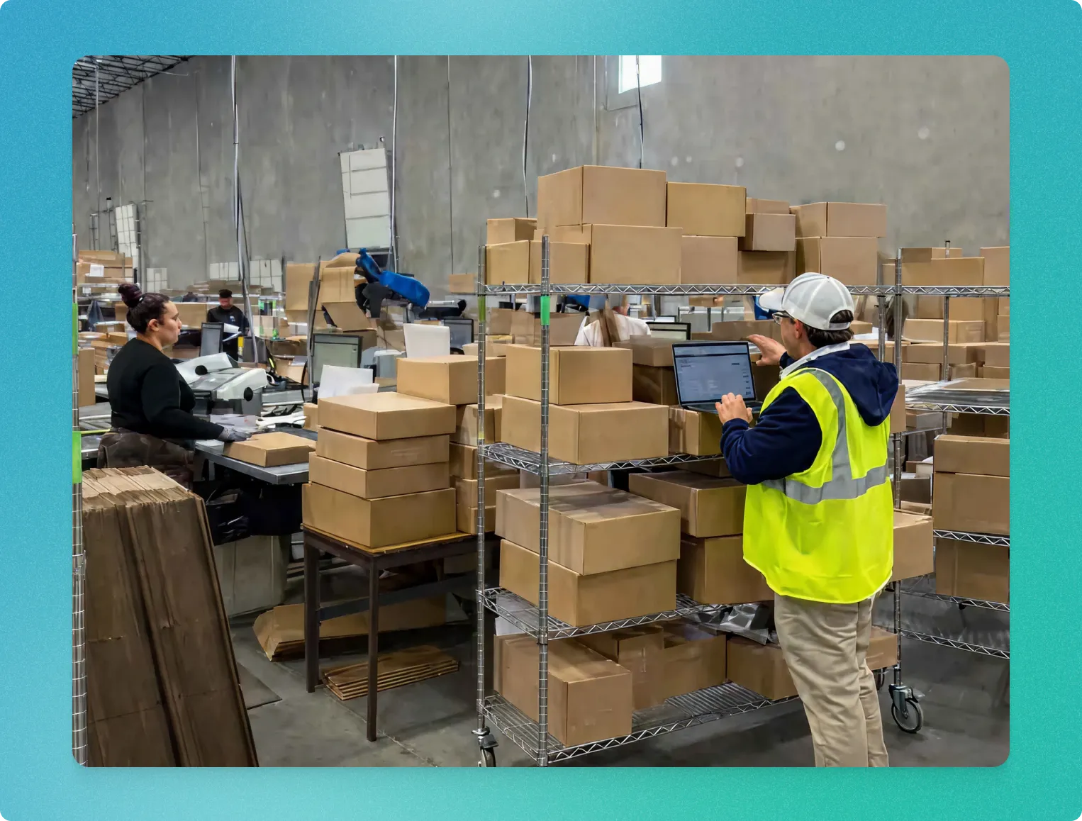 Warehouse workers handling and organizing cardboard boxes, one with a laptop checking inventory.