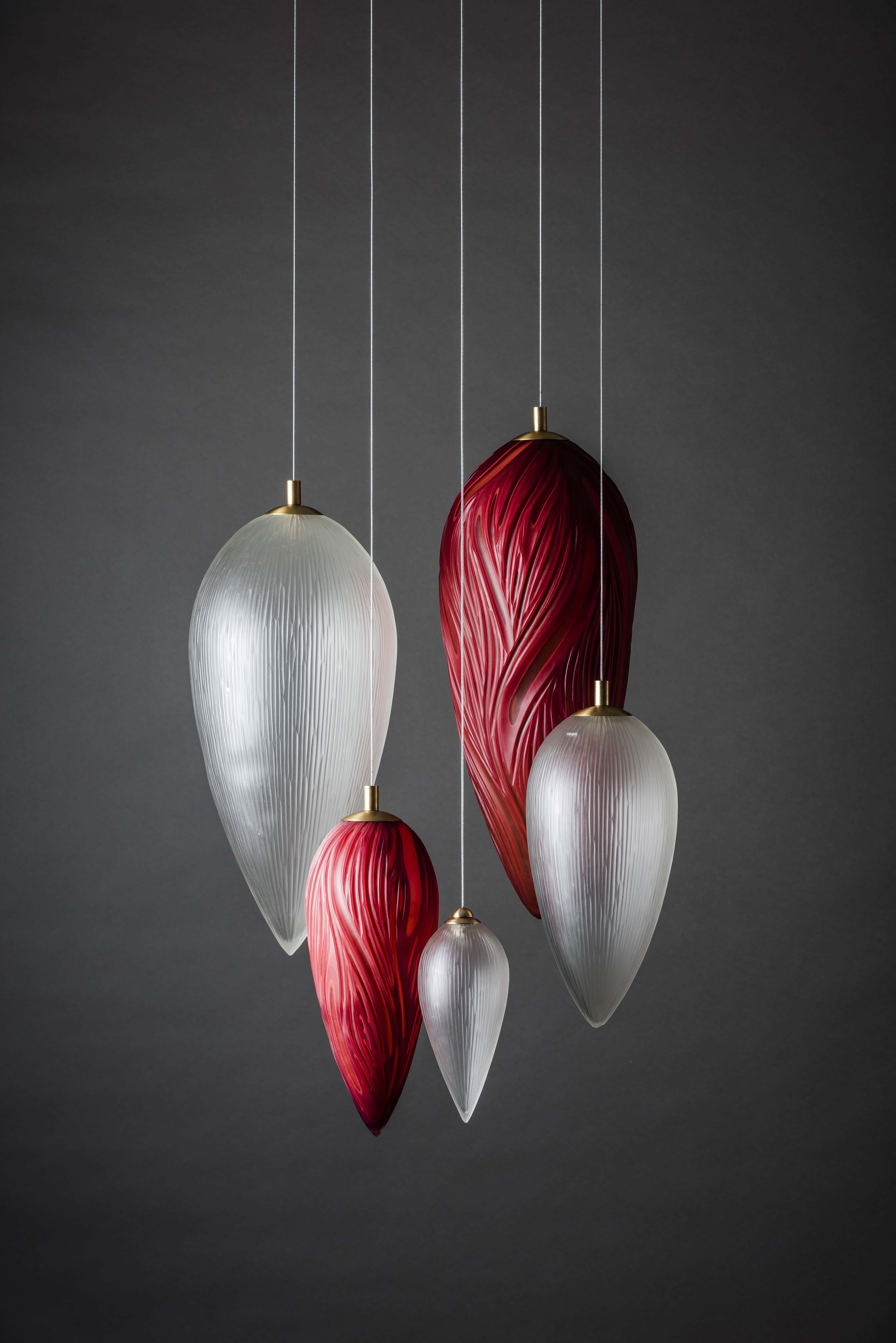 Cinq lampes suspendues en verre rouge et blanc avec motifs en relief sur fond gris.