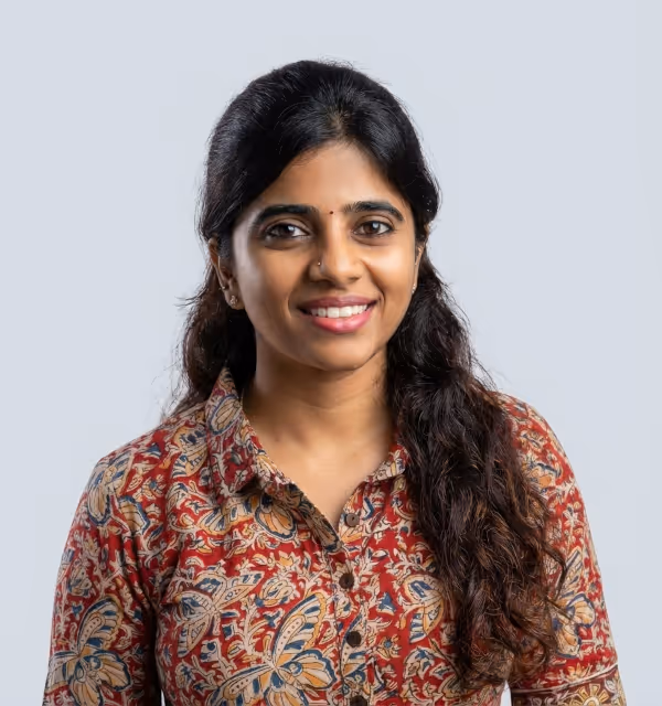 Smiling woman with long dark curly hair wearing a red patterned shirt against a light gray background.