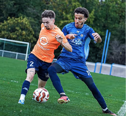 Two male soccer players in blue and orange jerseys competing for the ball on a grass field.