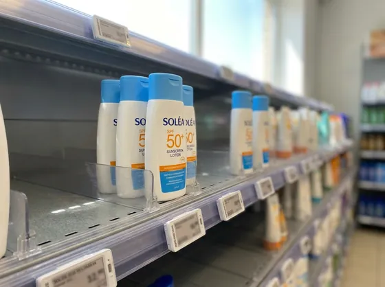 Rayon solaire d'un point de vente : flacons de crème solaire alignés sur l'étagère, avec des trous laissés par les ventes
