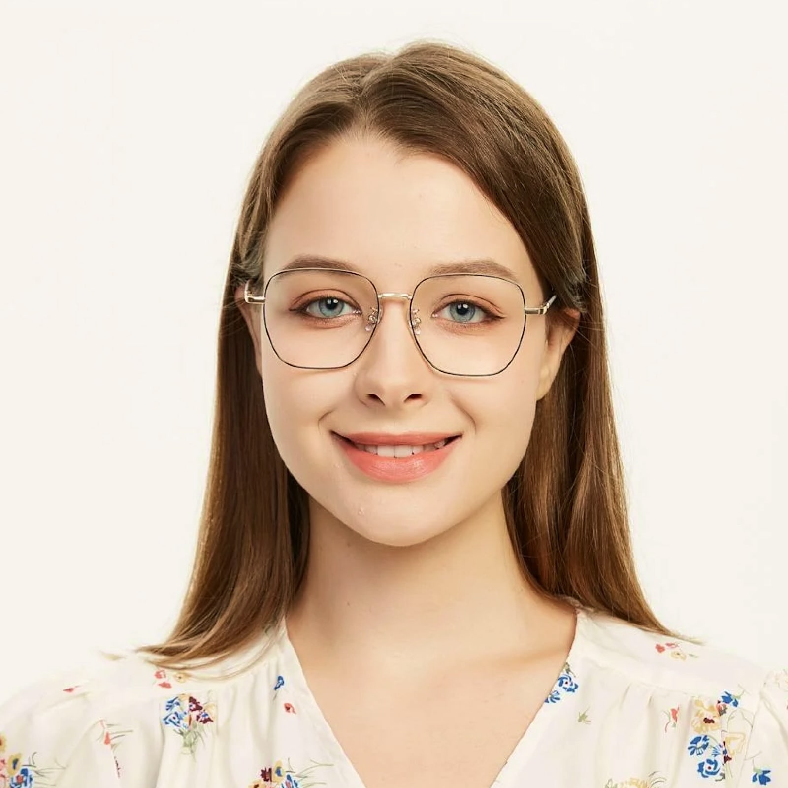 Smiling young woman with straight brown hair, wearing large thin-framed glasses and a white floral blouse.