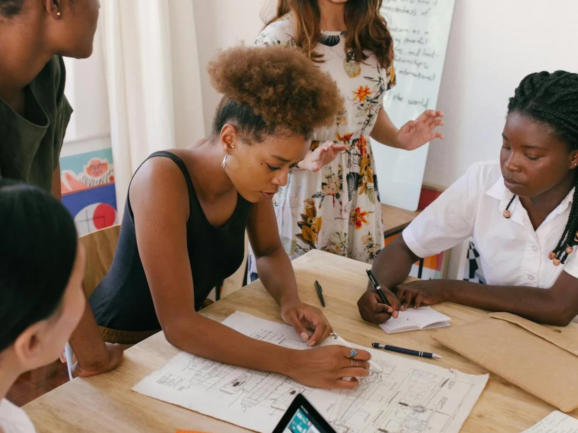 A group of young women collaborating around a table reviewing architectural blueprints and taking notes.