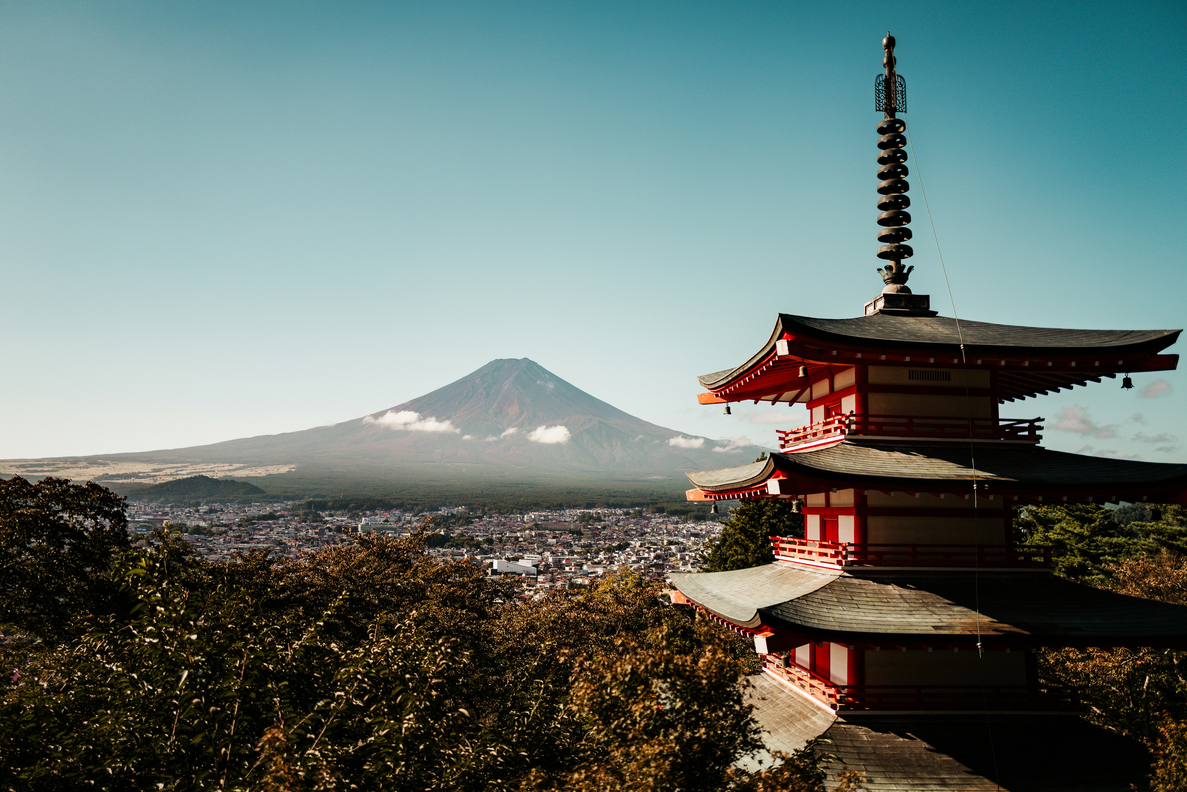 Chureito Pagoda in front of a cityscape with Mount Fuji and a clear blue sky in the background.