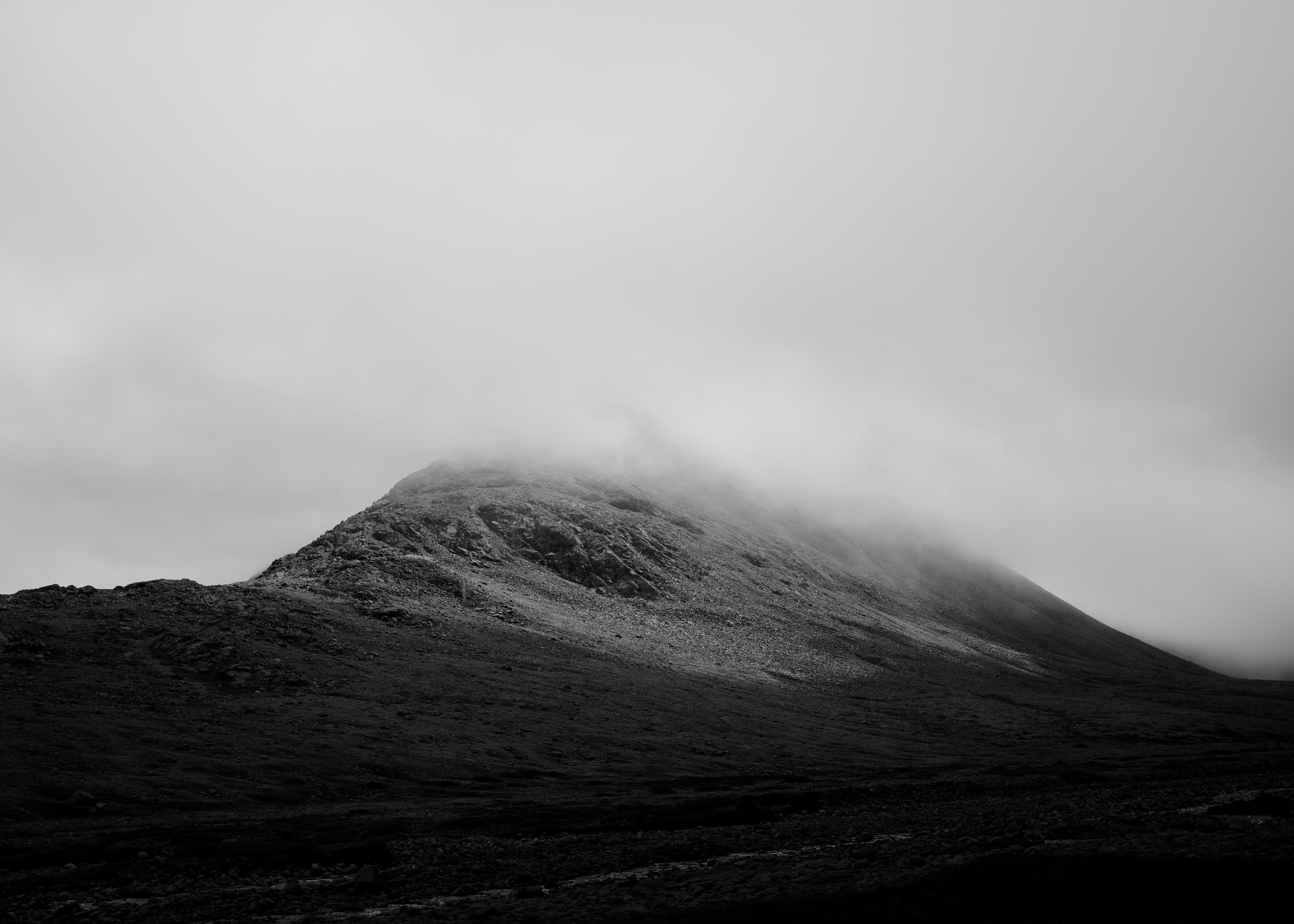 Fog partially covering a rocky mountain under an overcast sky in black and white.