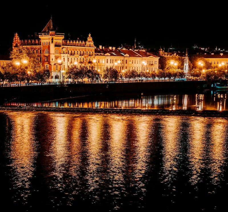 Ornate historic buildings illuminated at night reflecting on a calm river.