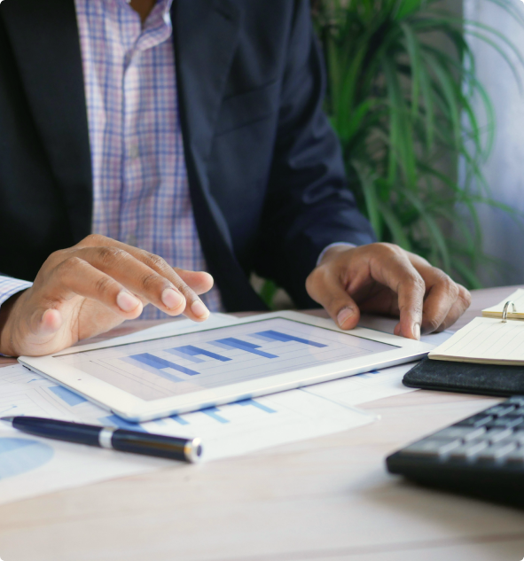 Person in business attire interacting with a tablet displaying a blue bar chart on a desk with documents, a pen, and a keyboard.