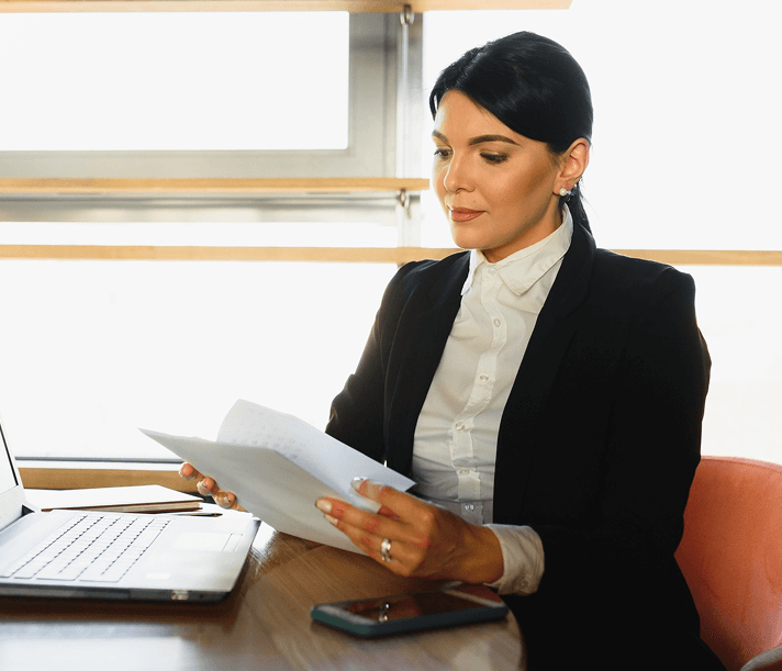 OpsMaven legal professional reviewing contract documents at a desk with a laptop in a modern office.