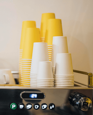 White ceramic mug with a tea bag on a wooden coaster on a gray table against a beige textured wall.