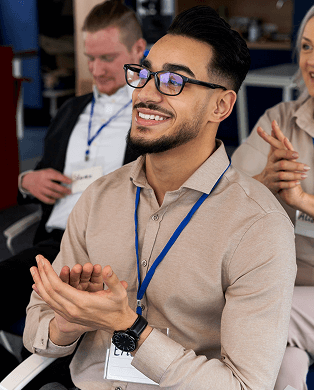 A woman with short blonde hair smiles and leans toward a seated woman with dark hair wearing a headset, who is typing on a keyboard.
