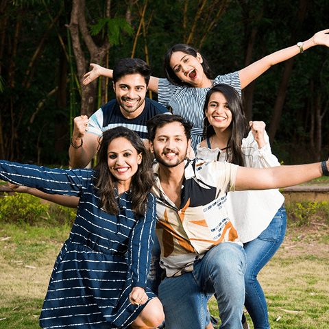 Five young adults smiling and cheering outdoors with trees in the background.