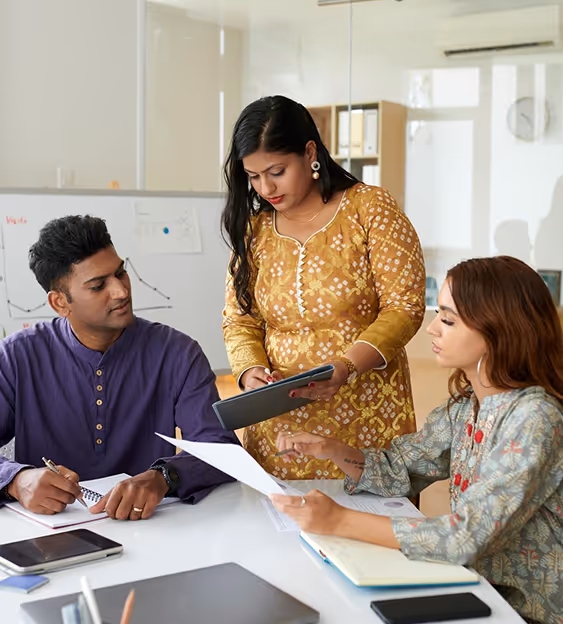 Three colleagues in traditional attire discussing documents in a modern office setting.