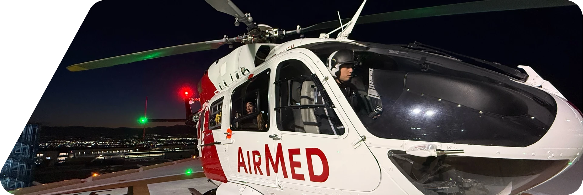 AirMed helicopter with medical crew on board parked on a helipad at night overlooking a cityscape.