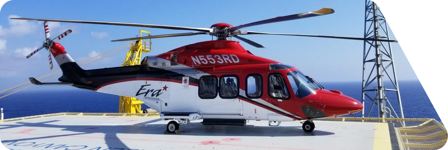 Red and white Era helicopter with registration N553RD parked on offshore helipad by the sea.