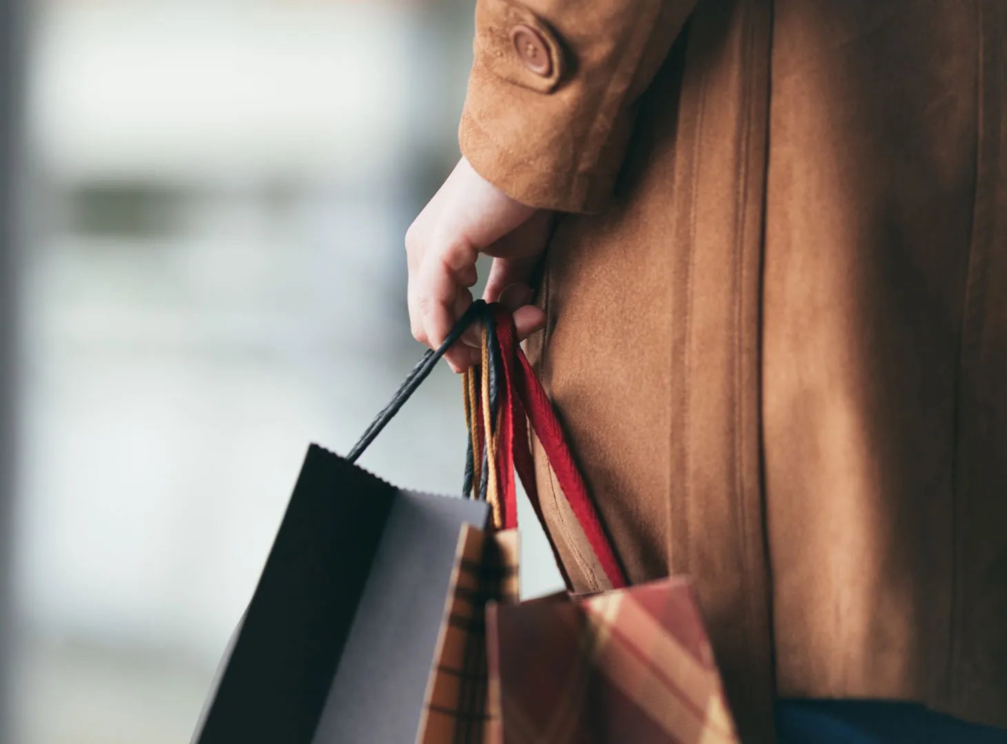 Une personne portant un manteau marron et tenant plusieurs sacs de courses à poignées colorées.