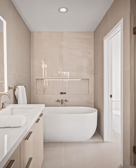 Modern bathroom with a white freestanding bathtub, beige tiled walls, and a vanity with a sink and towel.