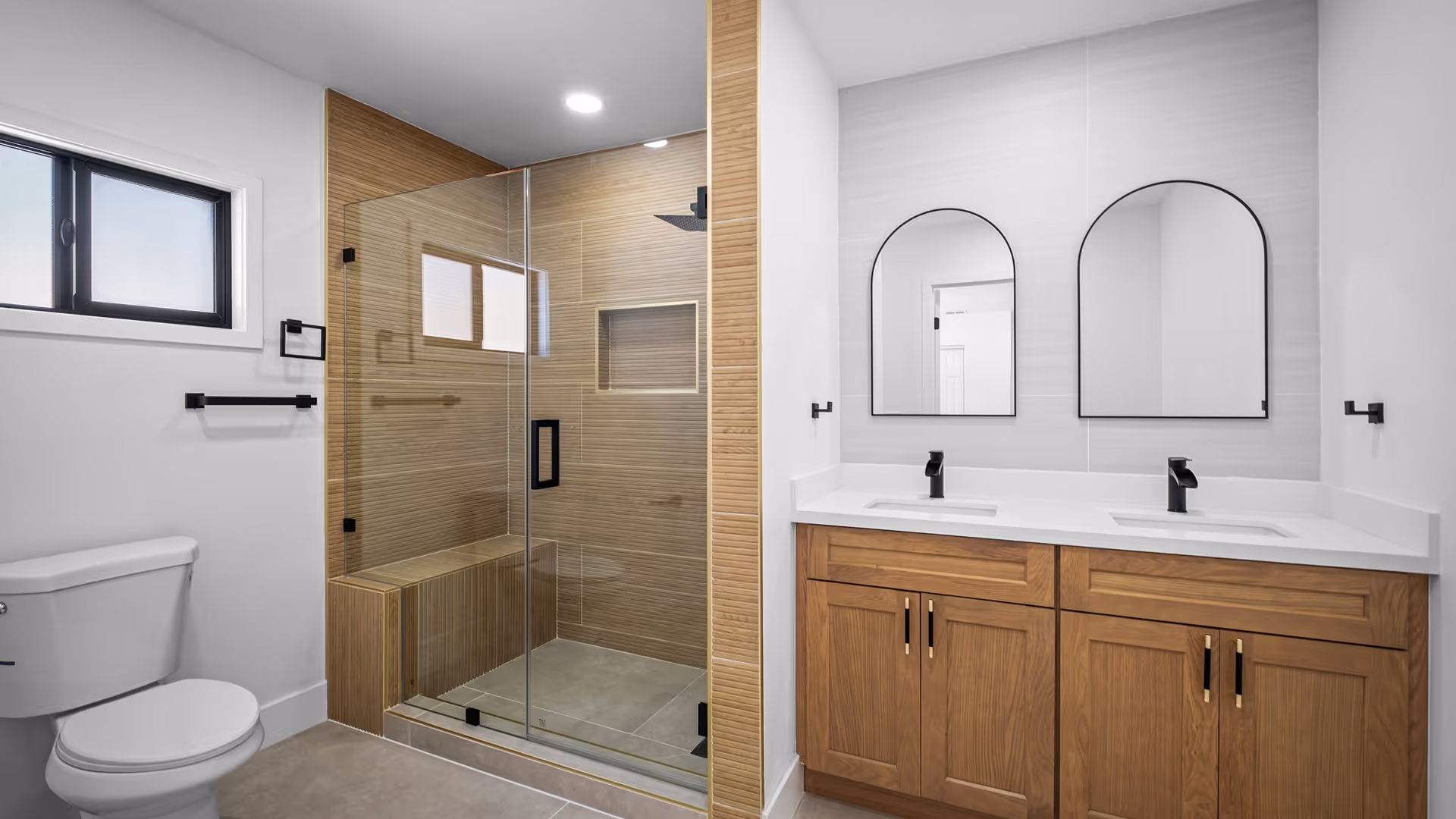 Modern bathroom with a glass-enclosed shower featuring wood paneling, a double sink vanity with wooden cabinets, and two arched mirrors.