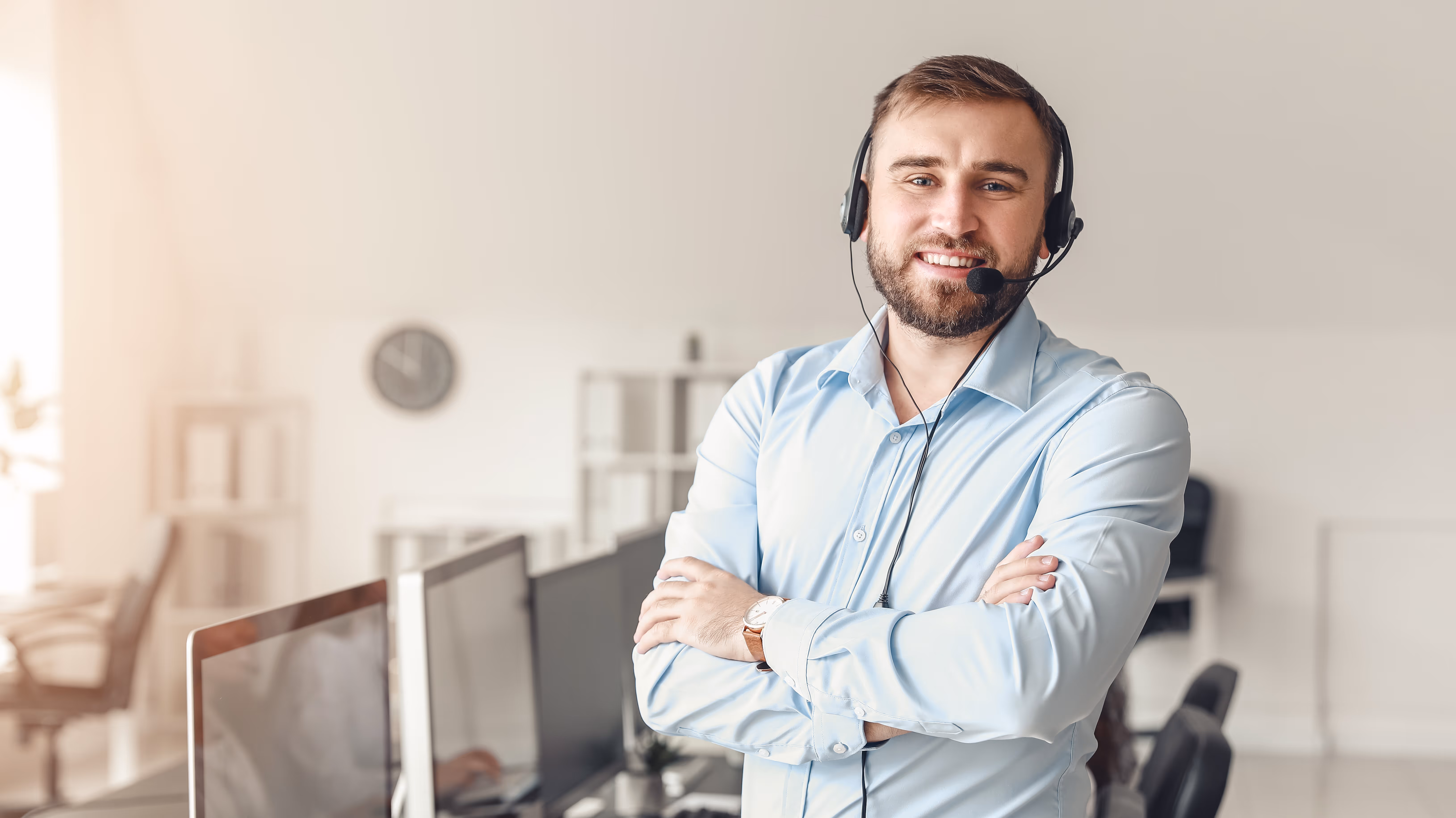 Smiling EDA support engineer wearing headset and blue shirt standing with arms crossed in a modern office.