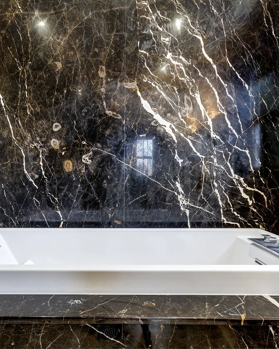 Dark veined stone behind a bath and across its surround