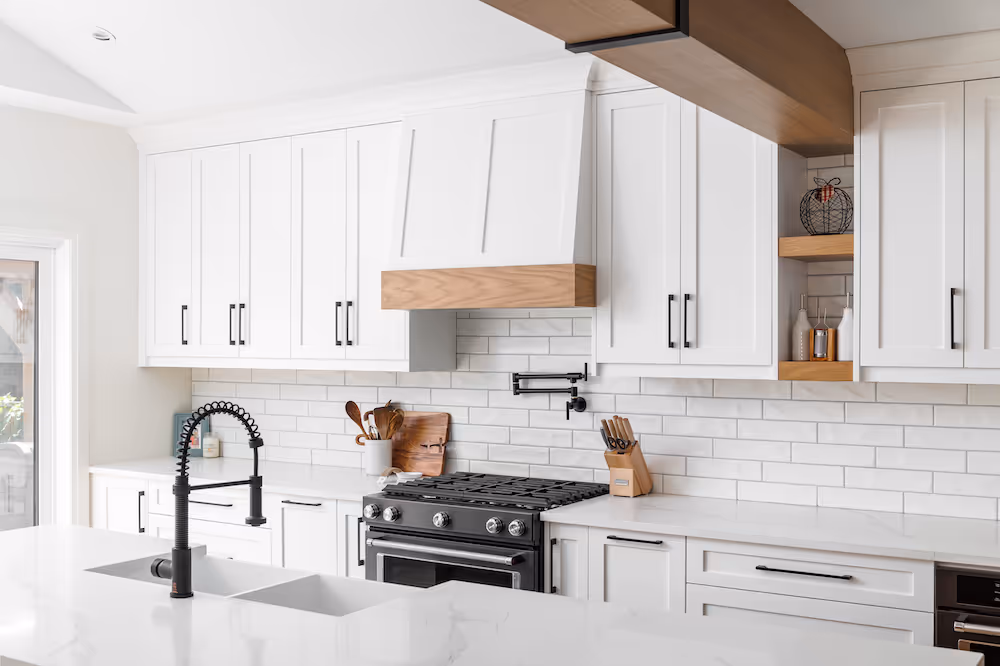 Modern white kitchen with black faucet, black stove, white cabinetry, subway tile backsplash, and wooden accents.