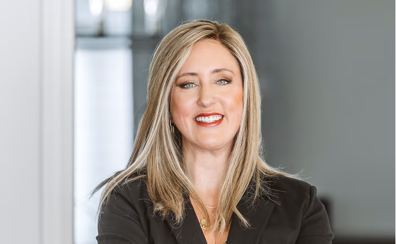 Smiling woman with blonde hair wearing a black blazer in a professional indoor setting.
