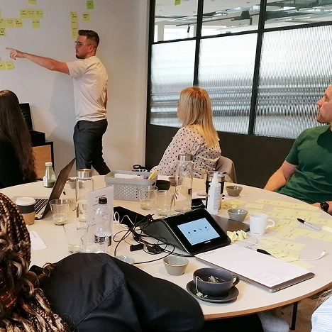 The 383 Group team working with Harley Davidson staff members. A man is stood at the end of the room pointing to post-it notes on a wall.