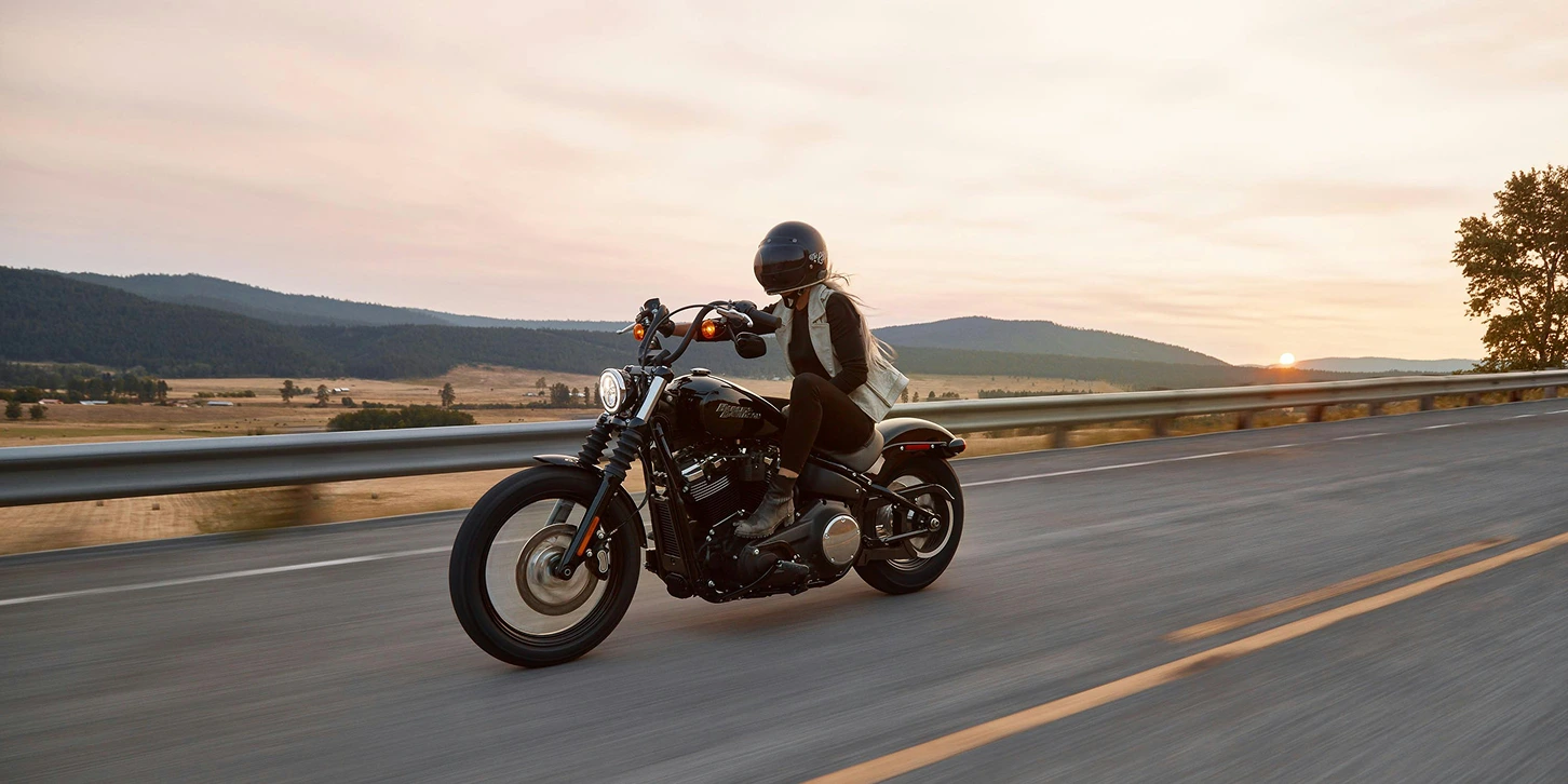 A lone female motorbike ride at sunset riding on a Harley Davidson. She has one hand on the handlebars and the other on her thigh. 
