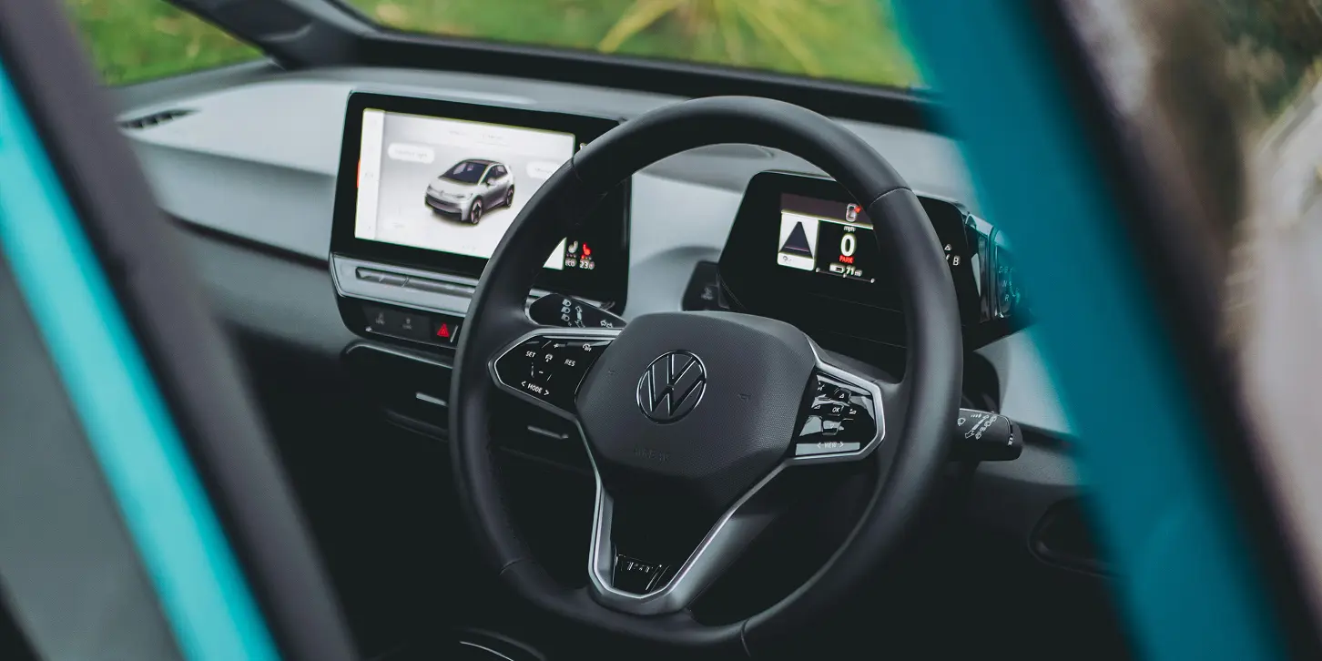 The interior of a VW i3. The image is shot from the open drivers door of a steering wheel and the central console screen is on showing the data from the car. 