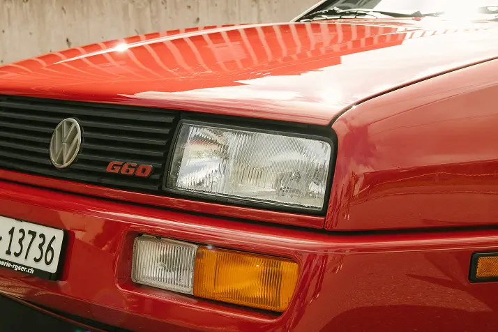 The front grill and bonnet of a classic, red VW Golf. Car is in front of a concrete background.   