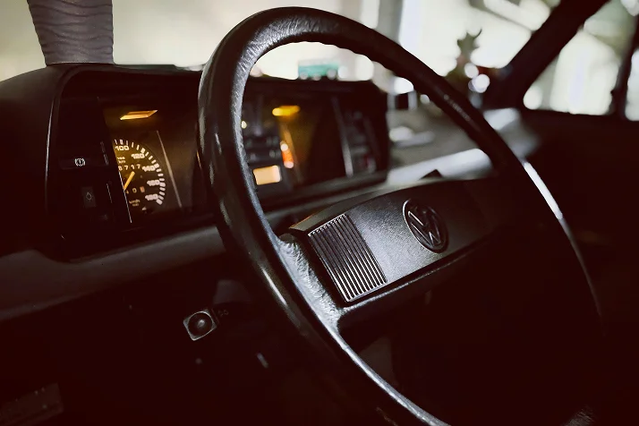 The black interior of a classic VW Golf from the 1980's. It is a left hand drive car with the dashboard dials lit up behind. 