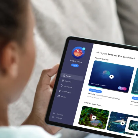 Person holding a tablet displaying a personalised educational app dashboard with marine learning videos and progress tracking.