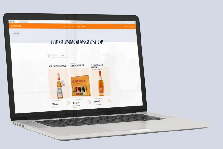 Open laptop displaying the Glenmorangie Shop website with whisky bottles and tasting gift sets for sale.