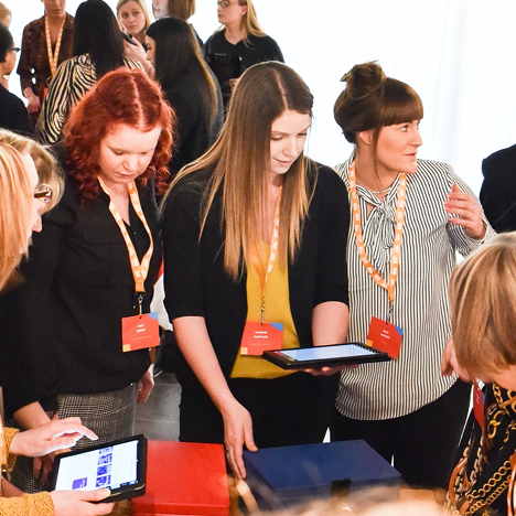 Group of people engaged in a discussion while holding tablets and wearing orange lanyards at a networking event.