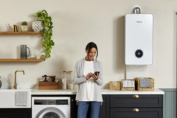 Woman standing in a modern kitchen looking at her smartphone next to a white wall-mounted boiler and washing machine.