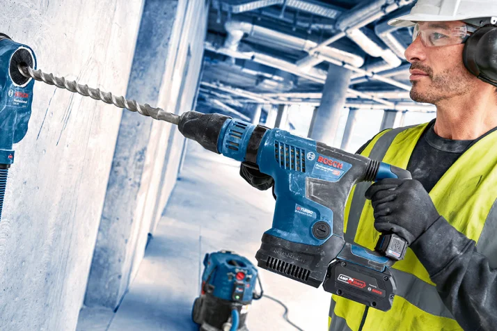 Construction worker in safety gear using a Bosch rotary hammer drill to drill into a concrete wall.