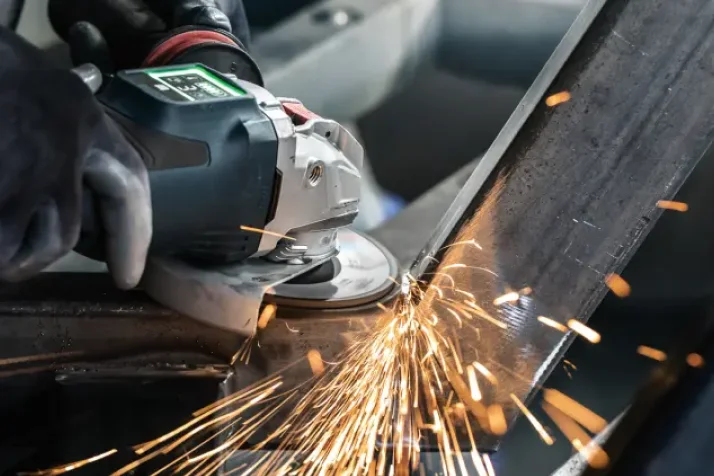 Close-up of a person using an angle grinder to cut metal, producing bright sparks.