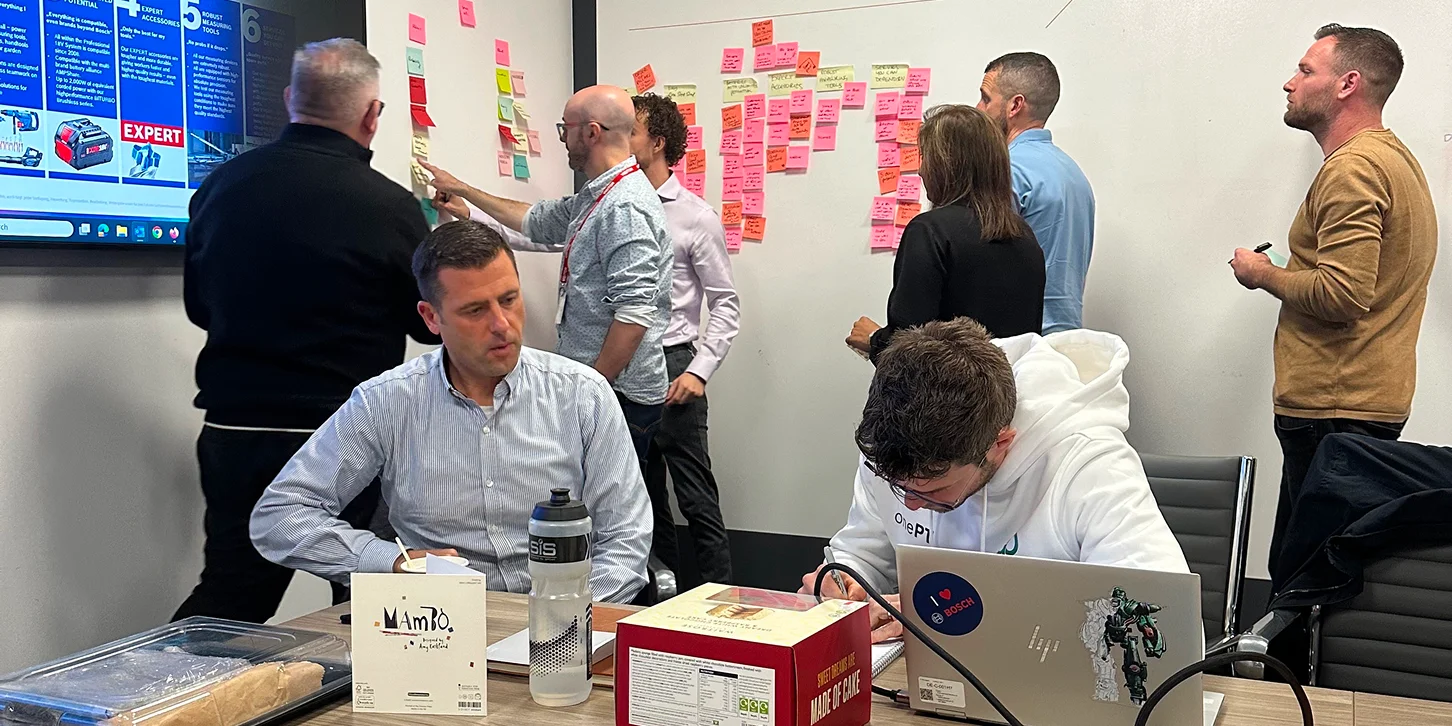 A group of professionals brainstorming in meeting room with sticky notes on wall and a digital screen displaying Bosch Power Tools content.