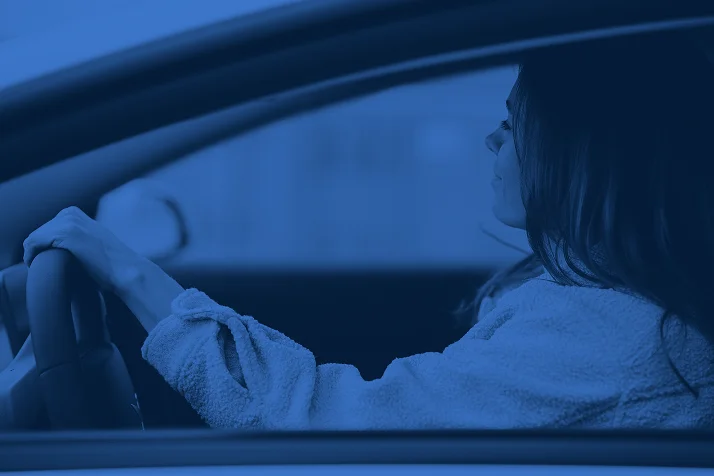 Woman driving a car, viewed from the side window, hands on the steering wheel.