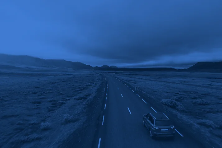Car driving on a winding road through a vast, empty landscape under a cloudy sky.