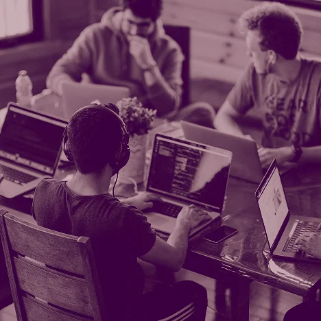 Group of people working on laptops around a table in a casual workspace.