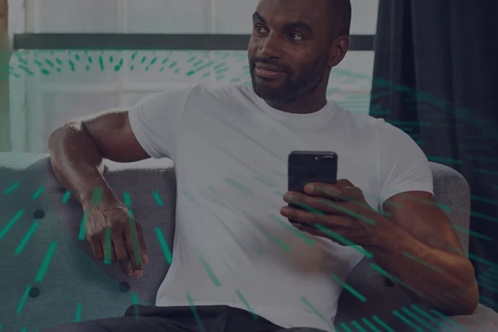 Man in a white t-shirt sitting on a couch looking to the side while holding a smartphone.