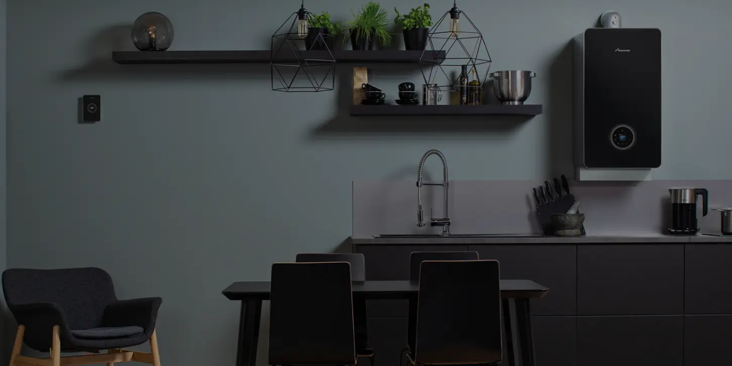 Modern kitchen with black dining table, four black chairs, gray armchair, minimalist shelves with plants and kitchen items, and a black wall-mounted boiler.