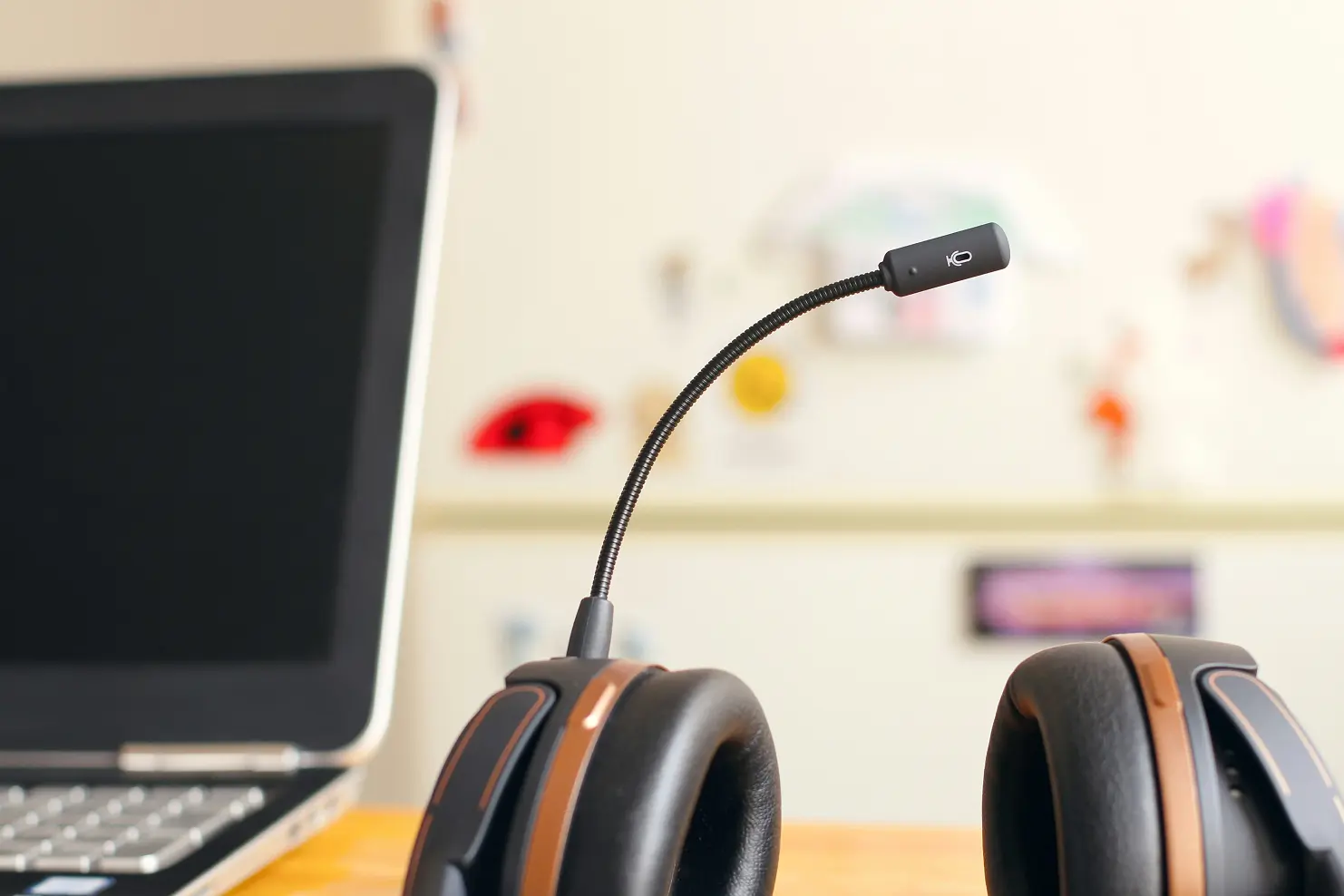 A set of headphones with microphone attached placed on a desk, in front of a computer in a workplace.